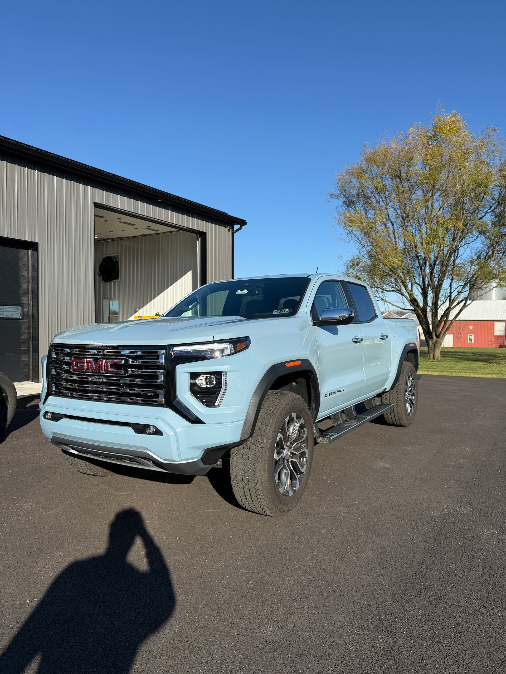 Light blue GMC Canyon truck parked in front of a gray building on a sunny day.