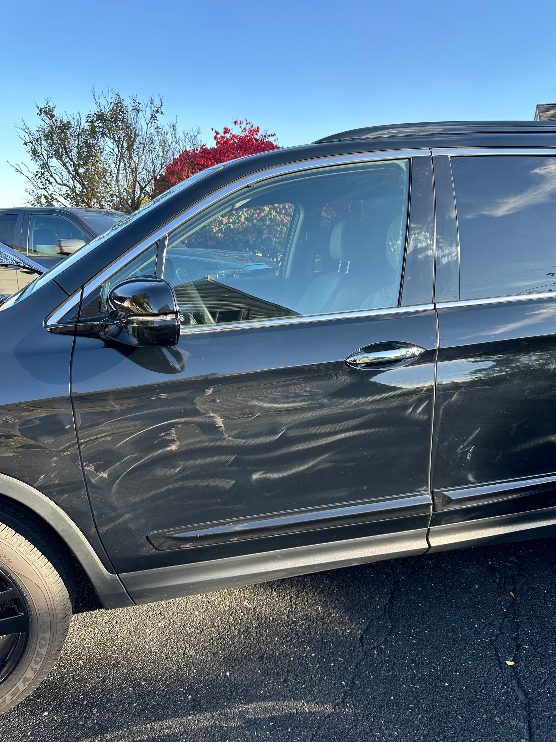 Dark SUV with swirl marks on the side, parked outside on a sunny day.