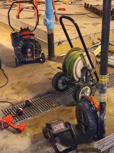 Tools for drain cleaning in a construction area: reel, drain cleaners, and cordless drill.