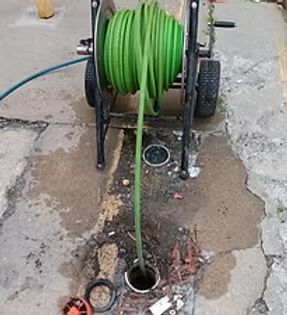 Green hose extending into a drain, attached to a reel cart on a concrete surface.