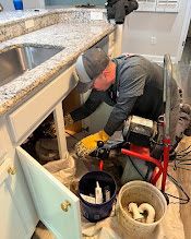 Green hose extending from a reel into a sewer drain in a concrete area.