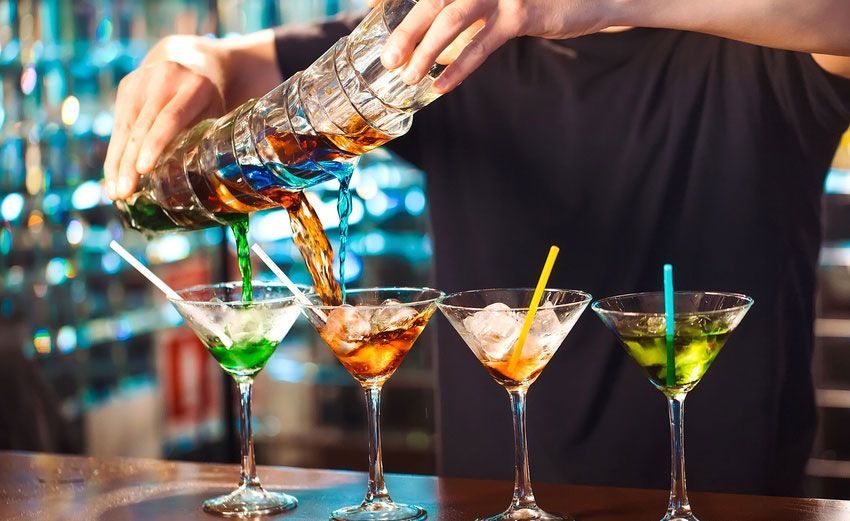 A bartender is pouring a drink into a martini glass.