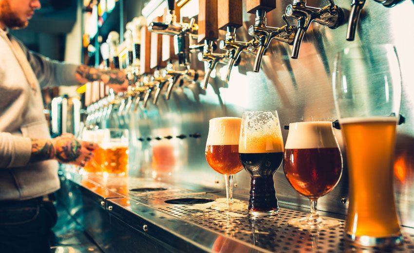 A bartender is pouring beer into glasses at a bar.