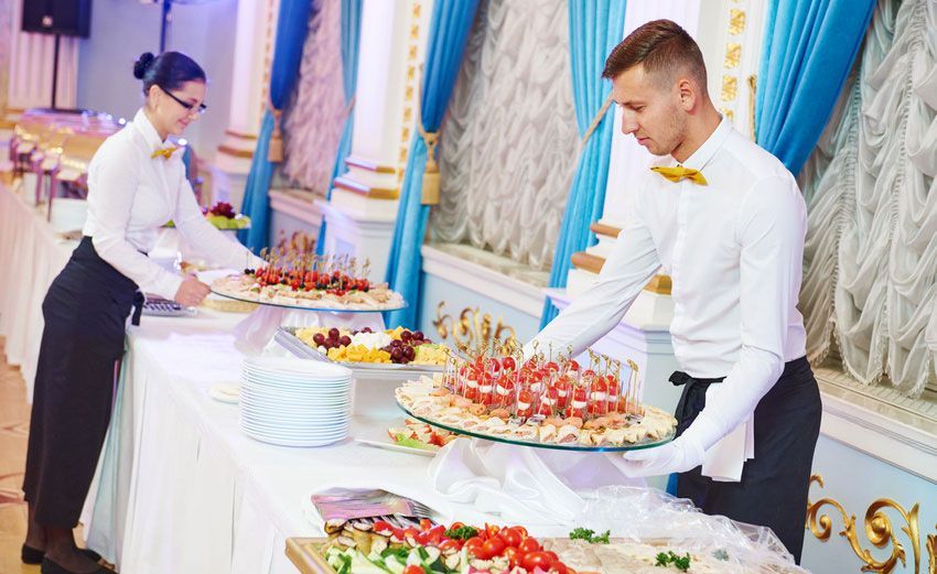 A man and a woman are serving food at a buffet table.