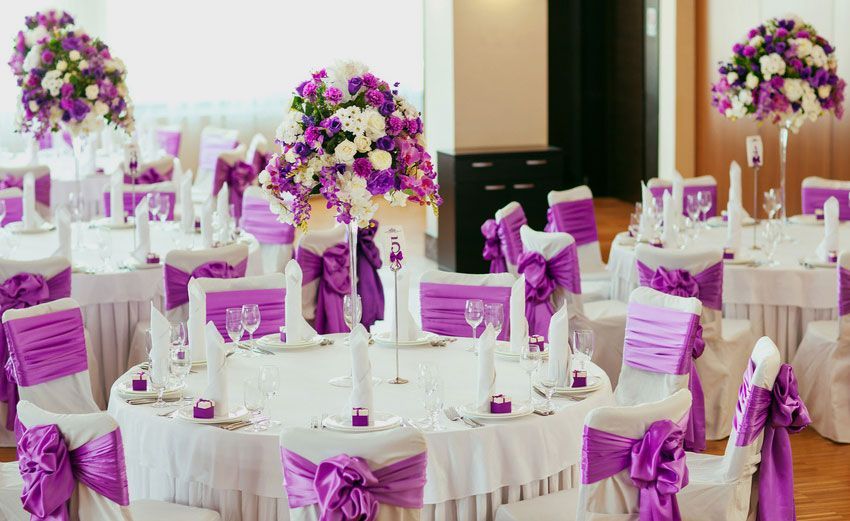 A room filled with tables and chairs decorated in purple and white for a wedding reception.