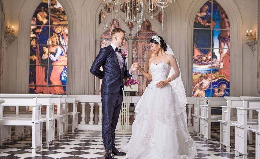 A bride and groom are standing in front of a stained glass window in a church.