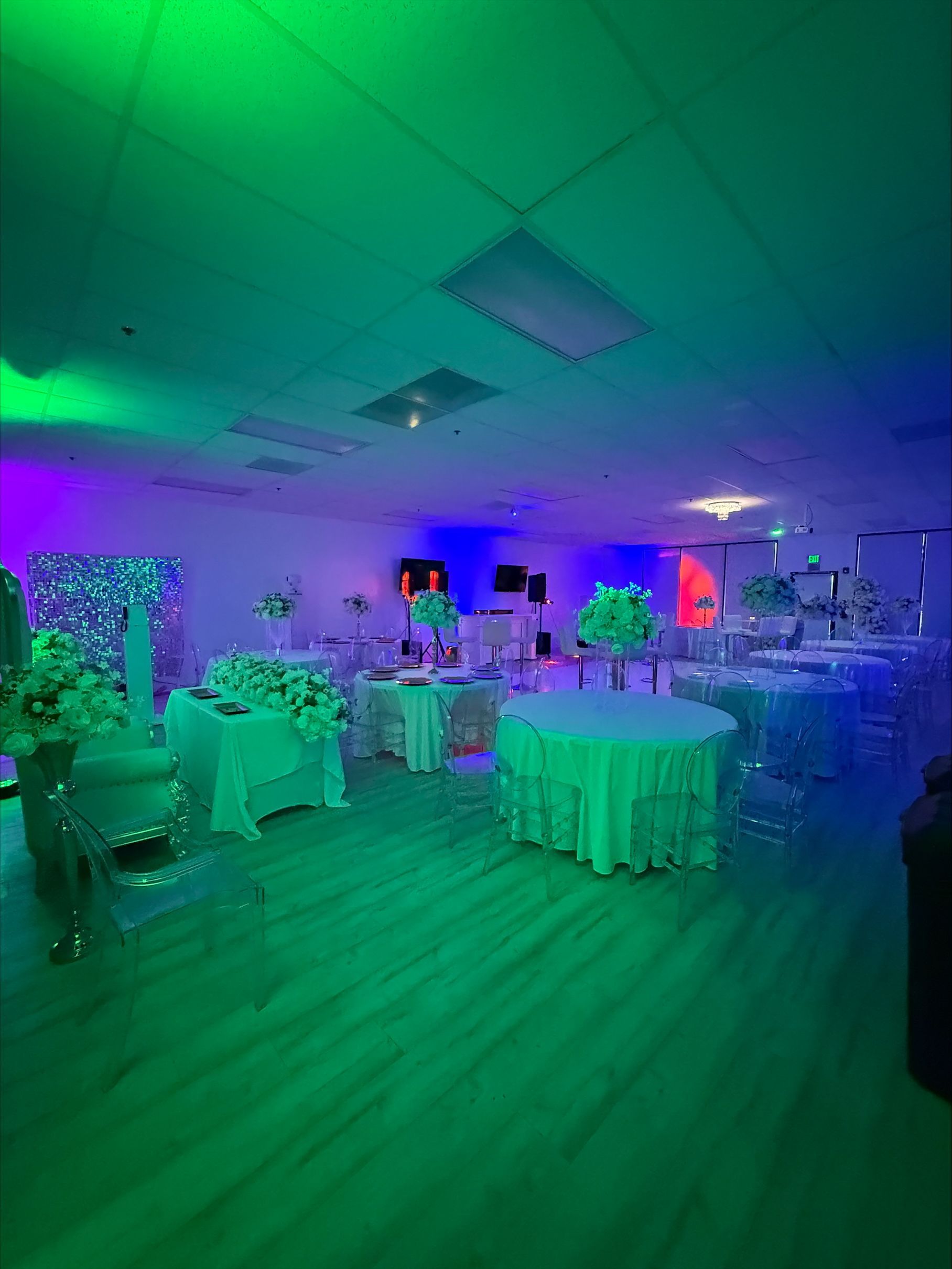 A large room filled with tables and chairs is lit up with green and purple lights.