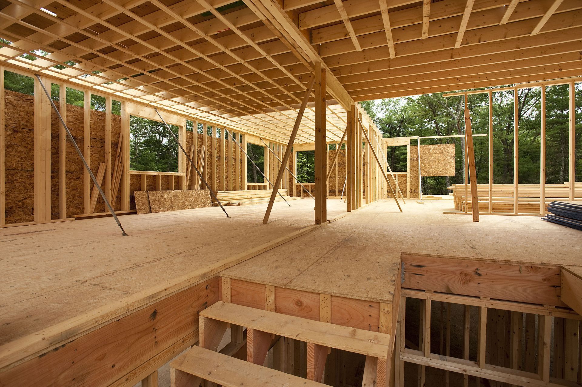 Wooden house frame under construction; interior view with stairs and open spaces.