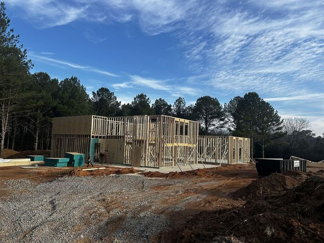Two-story house under construction, exposed wooden frame against a clear blue sky.