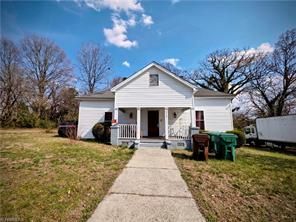 A white, single-story house with a front porch and walkway, centered in a yard with trees under a blue sky.
