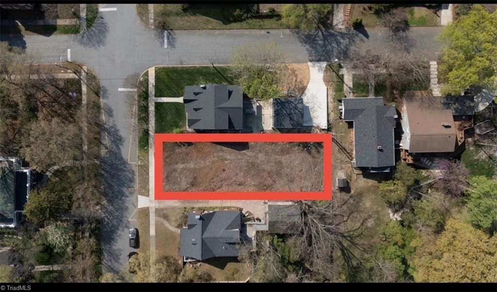 Aerial view of a rectangular, vacant grass lot highlighted in red, situated between two houses on a residential street.