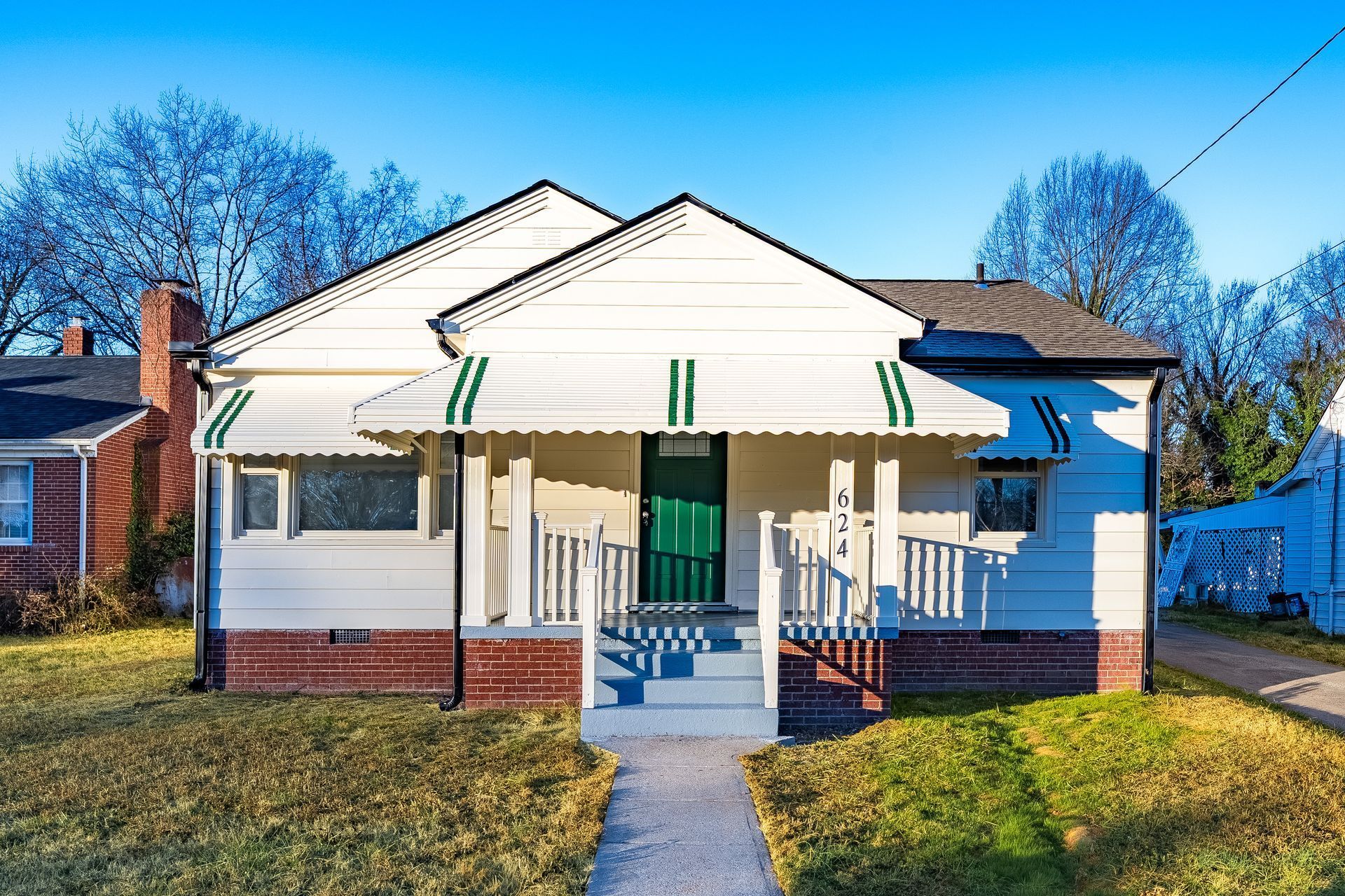 Cottage-style home with white siding, brick base, green door, awning, and small front porch