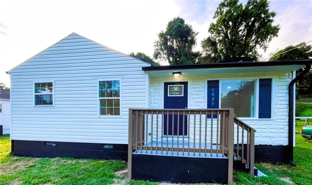 White house with a dark blue door and windows, small wooden porch. Green grass and trees in the background.