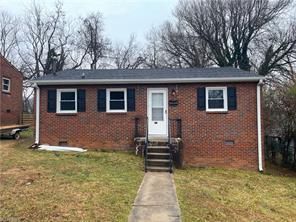 Red brick house with black shutters, white trim, and a concrete path leading to the front door