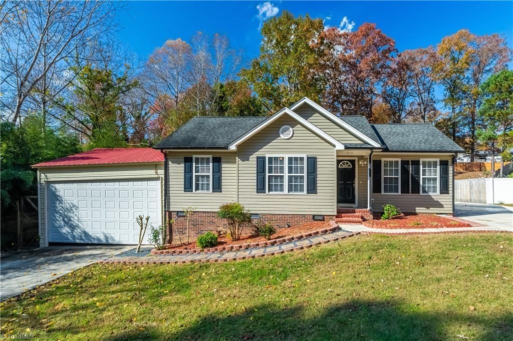 Beige house with attached garage, landscaping, and fall trees against a blue sky