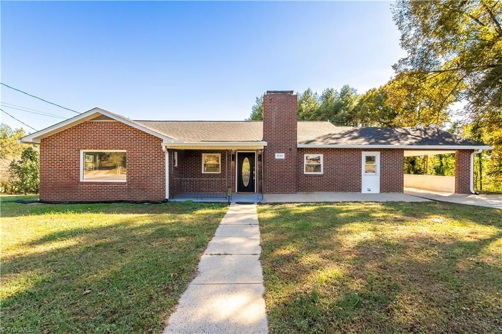 Brick ranch house with a carport, chimney, and a walkway leading to the front door.