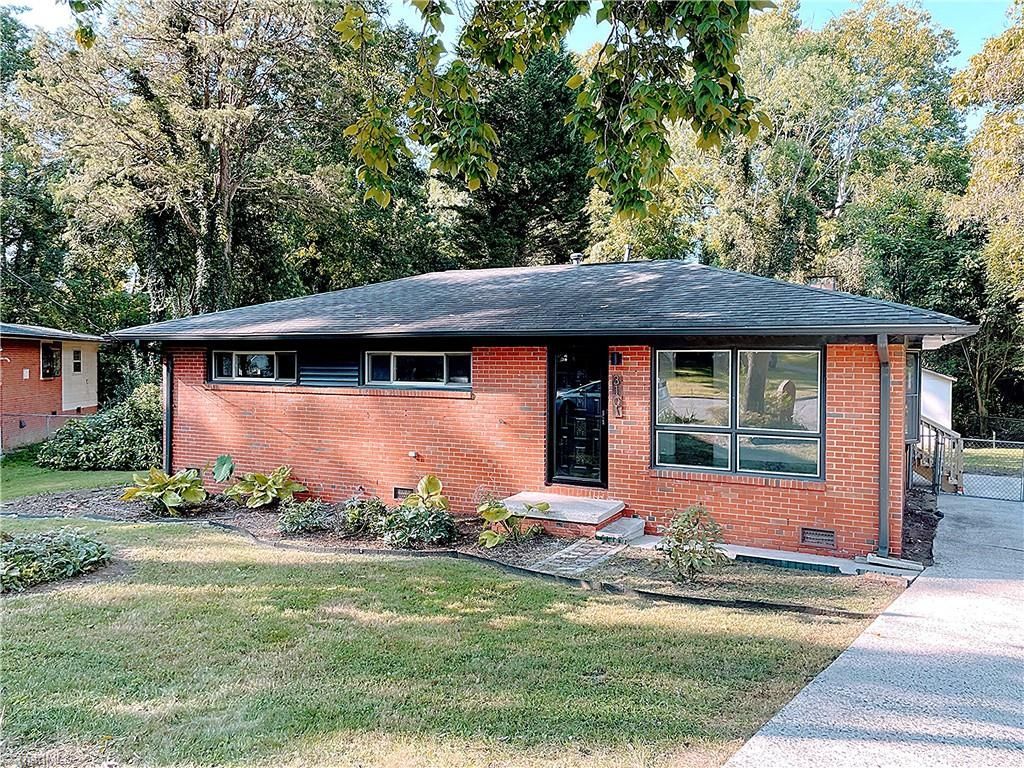 Brick ranch-style house with a dark roof, surrounded by trees and a small lawn