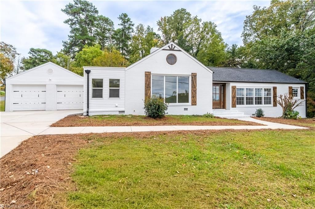 White house with attached two-car garage. Brown trim, large windows, green lawn, trees in background.