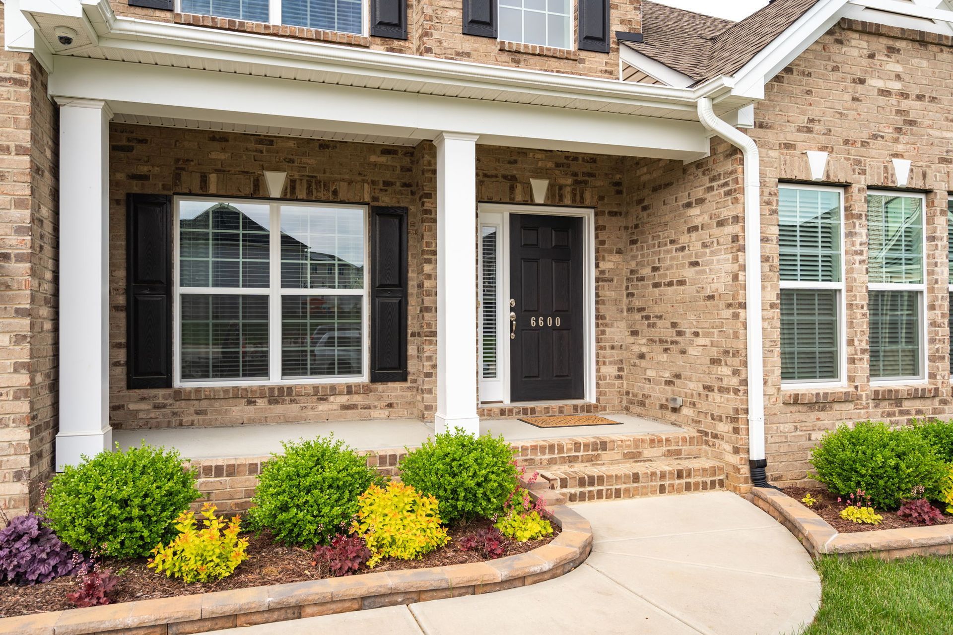 A brick house with a large porch and a black door.