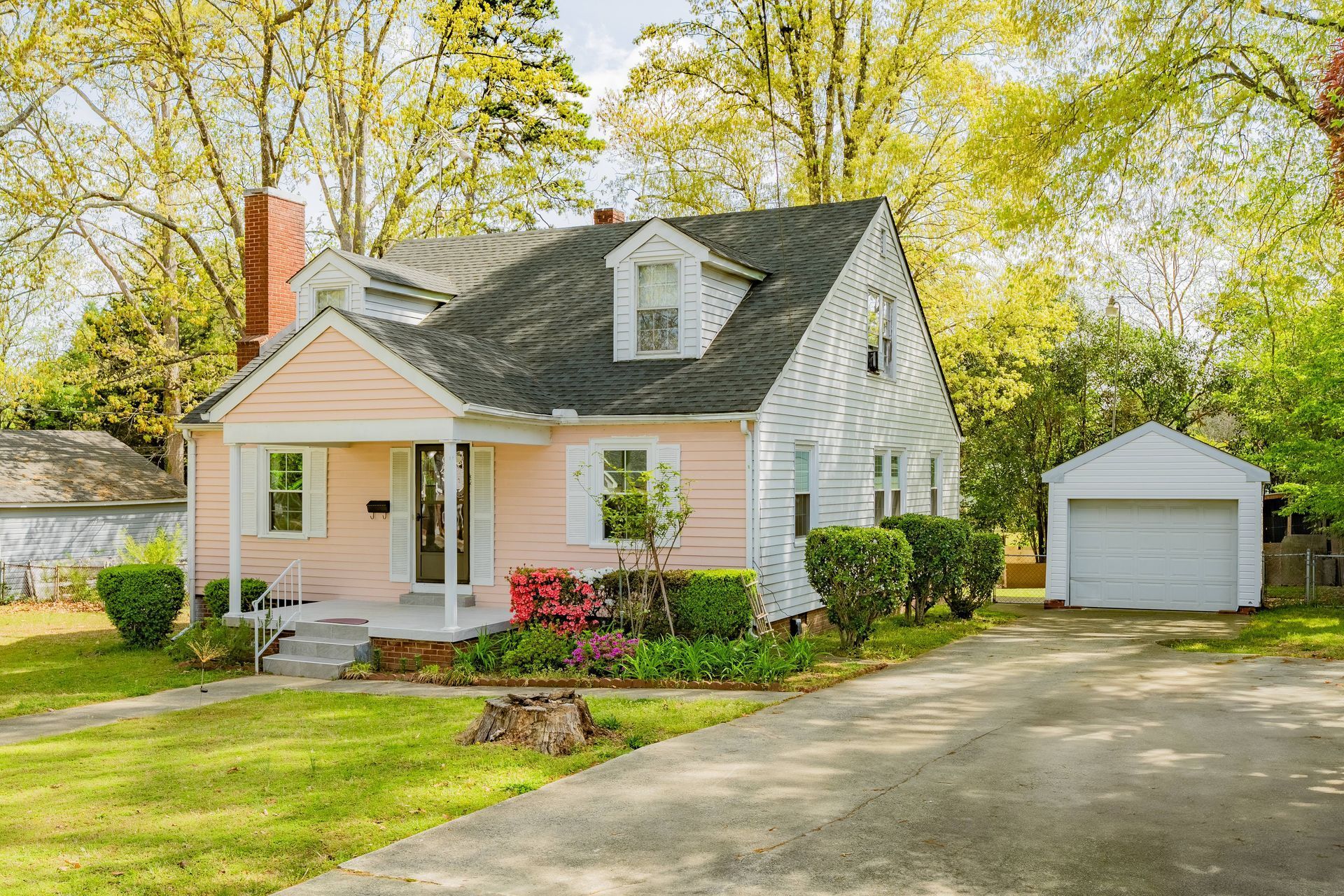 A pink and white house with a black roof and a garage.