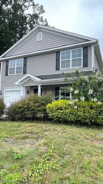 Two-story gray house with black shutters. Overgrown green bushes in front.