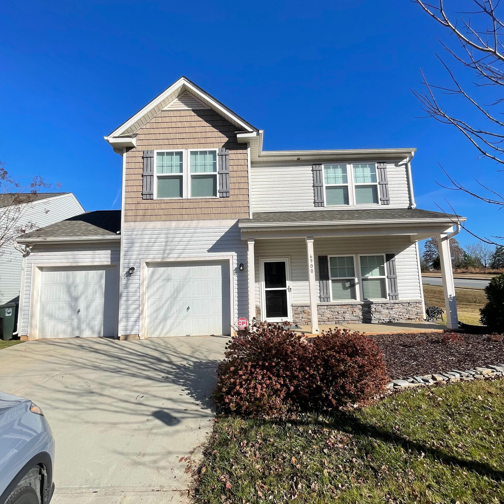 Two-story house with a porch, attached garage, and blue sky.