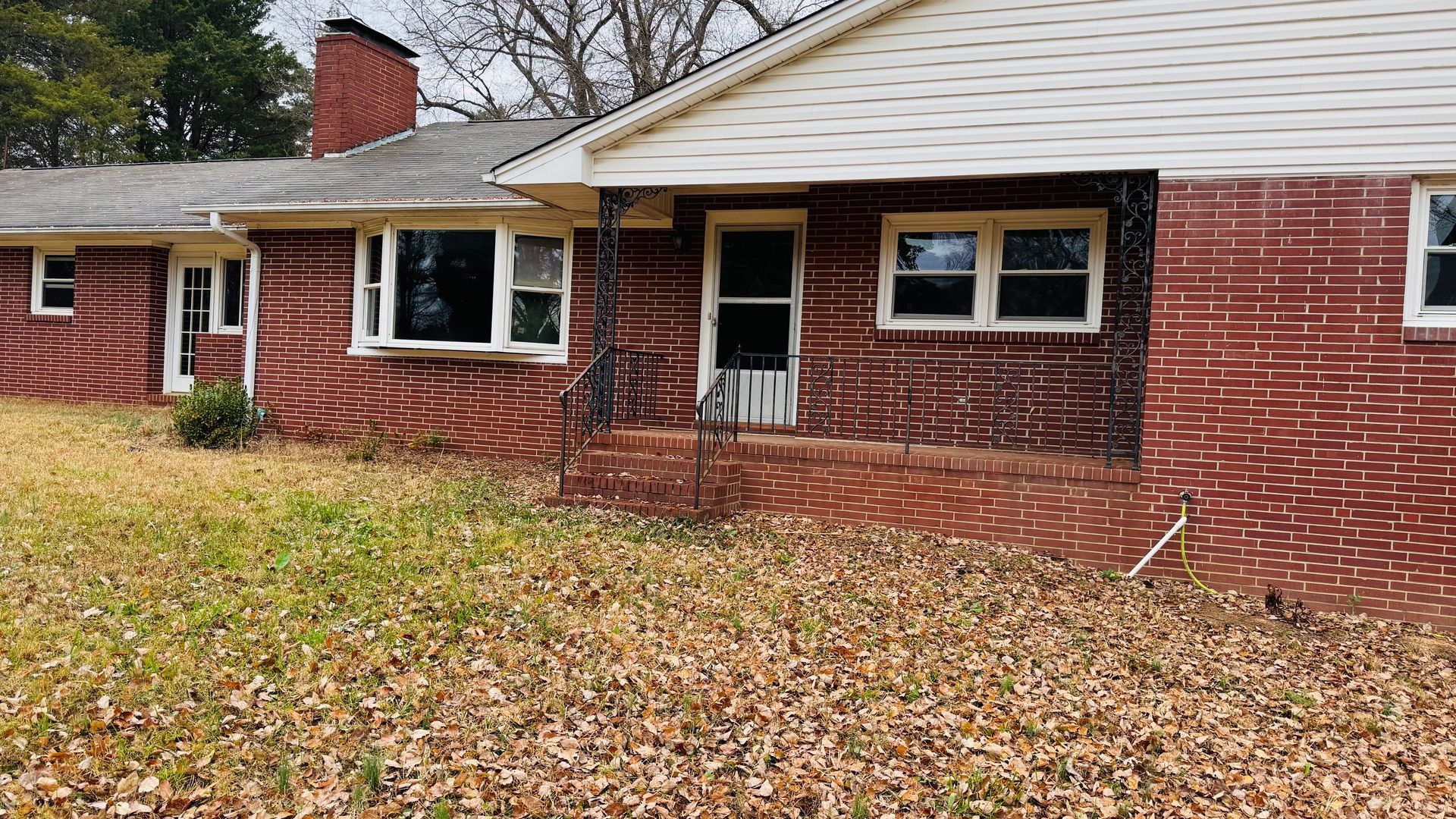 Brick house with a brown roof and overgrown grass.
