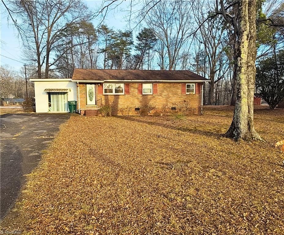 Brick ranch house with attached garage and driveway, in a yard covered in fallen leaves, under a blue sky.