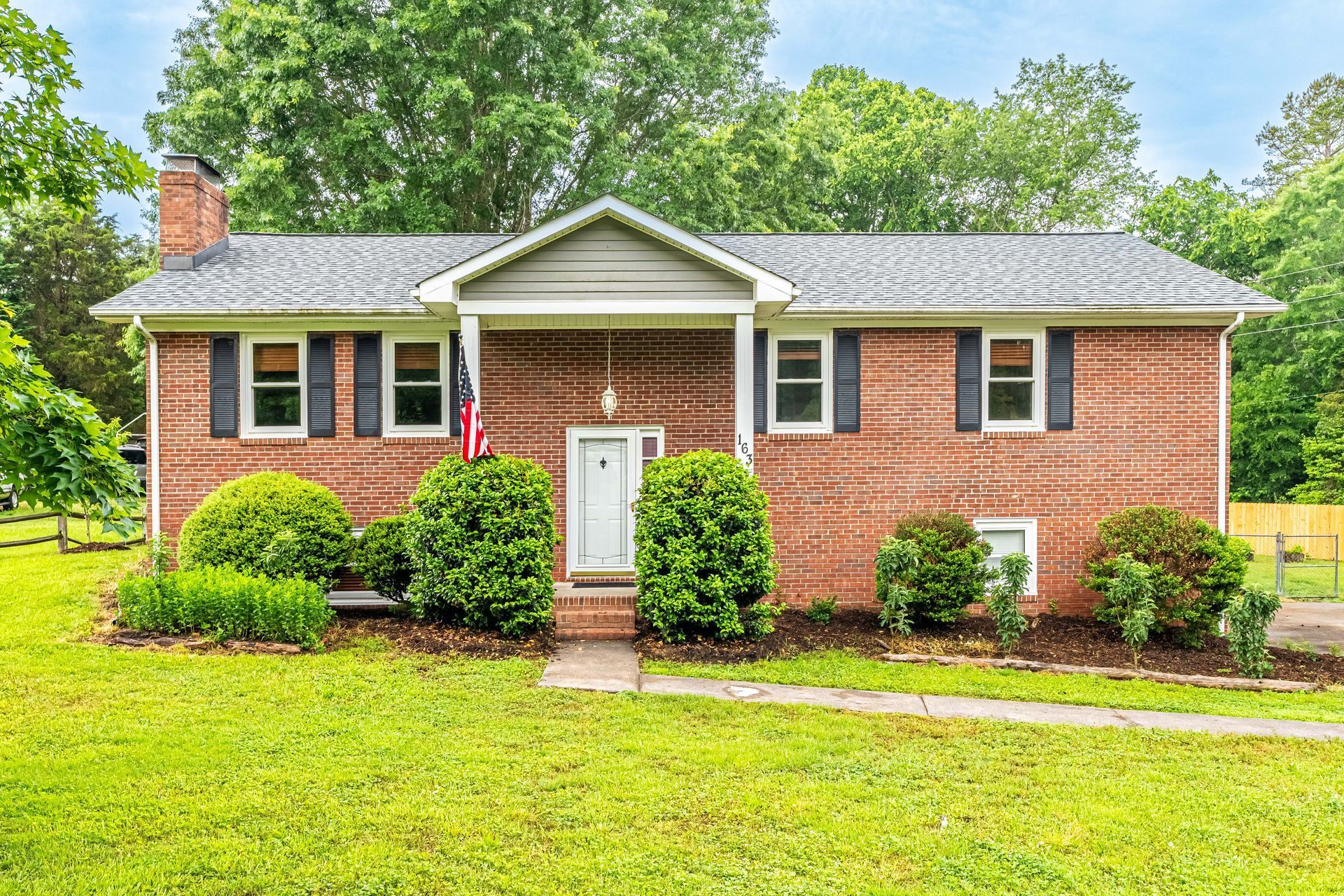 A brick house with black shutters and a large lawn in front of it.