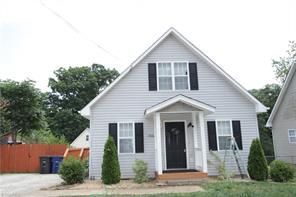 Light gray house with black shutters and door, small porch, two trees, and grassy yard.