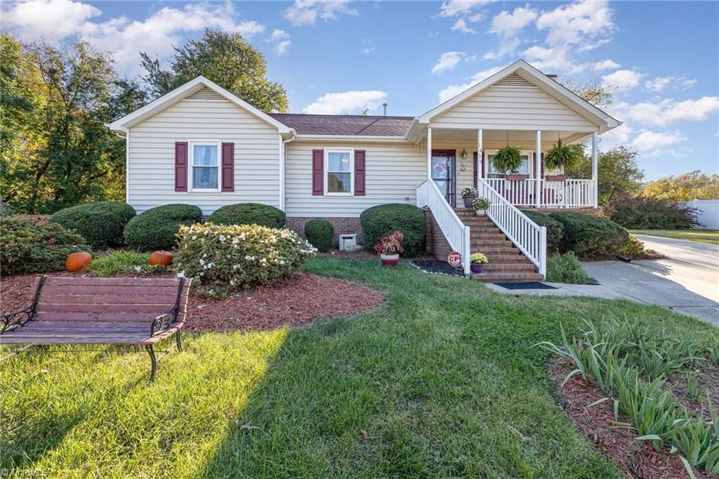Tan ranch-style house with a porch, red shutters, and a green lawn under a blue sky.