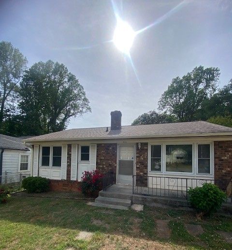 Single-story brick and white house with front porch, lawn, and bright sun overhead