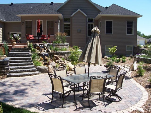 A patio with a table and chairs and an umbrella in front of a house