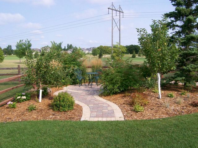A brick walkway leading to a patio with a table and chairs