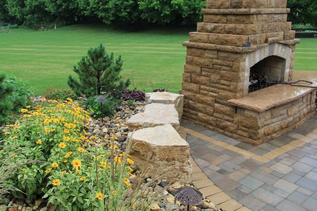A stone fireplace is sitting on a patio next to a lush green field.