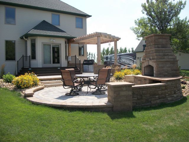 A patio with a table and chairs and a fireplace in front of a house