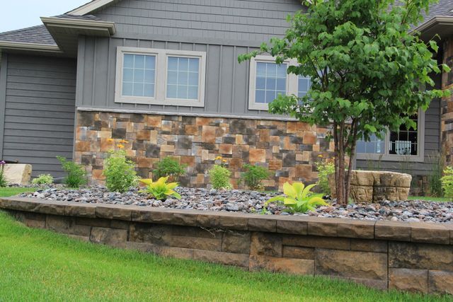 A house with a stone wall and a tree in front of it.