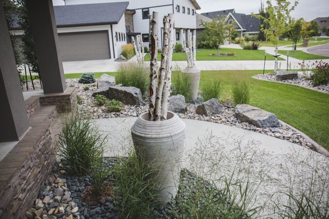 A large vase filled with sticks is in the middle of a garden in front of a house.