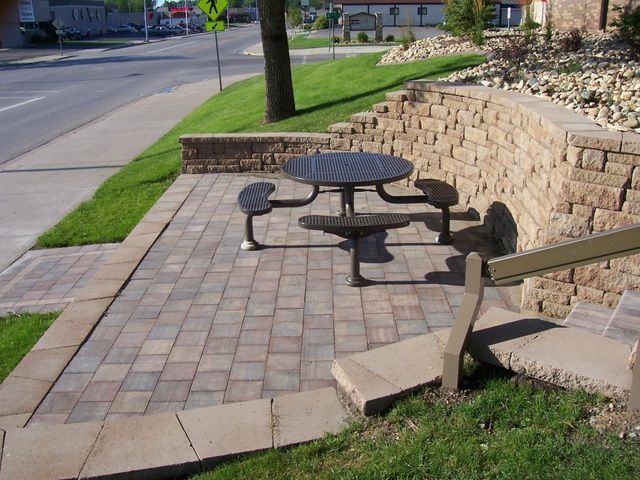 A picnic table sits on a sidewalk next to a brick wall