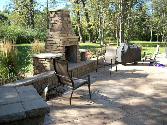 A patio with a stone fireplace and chairs
