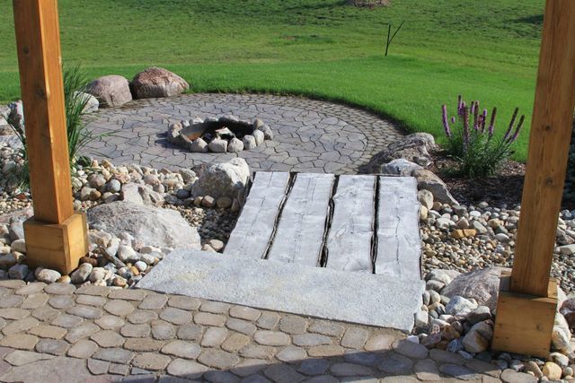 A stone walkway leads to a fire pit in the middle of a garden.