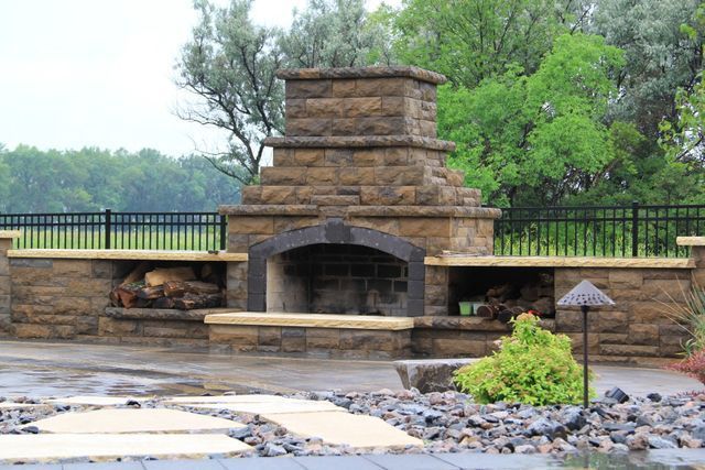 A large stone fireplace in a backyard with a fence in the background.