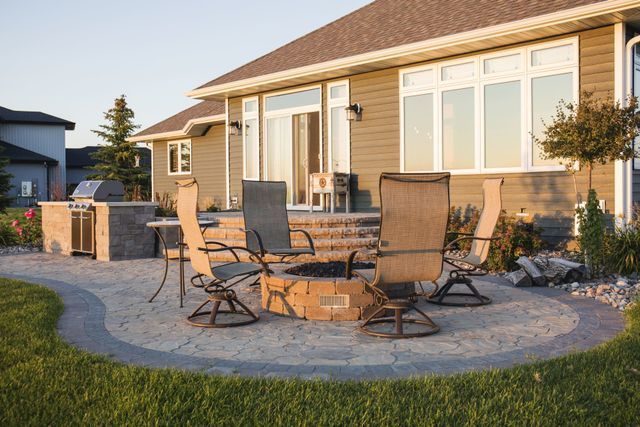 A patio with a fire pit and chairs in front of a house.