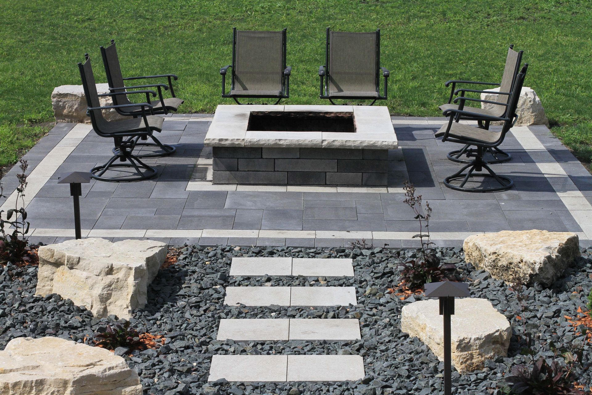 A fire pit in the middle of a patio with chairs around it