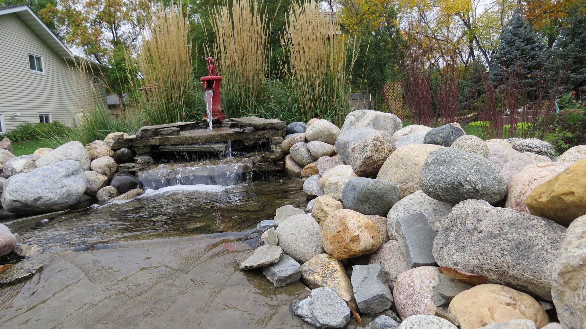 A waterfall is surrounded by rocks and a house in the background.
