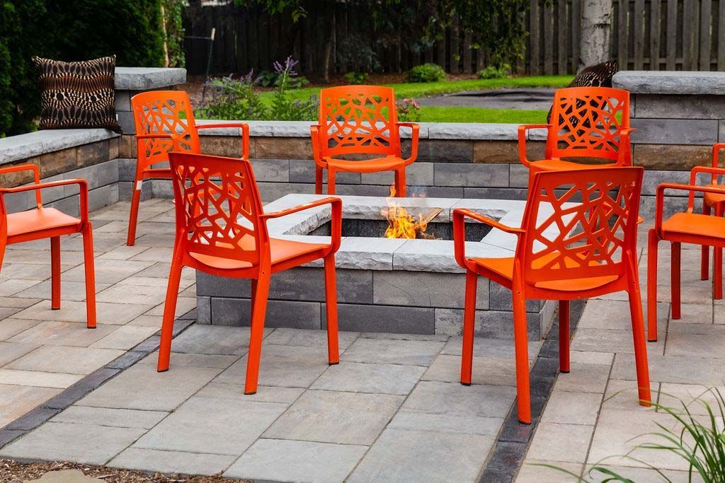 A group of orange chairs are sitting around a fire pit on a patio.