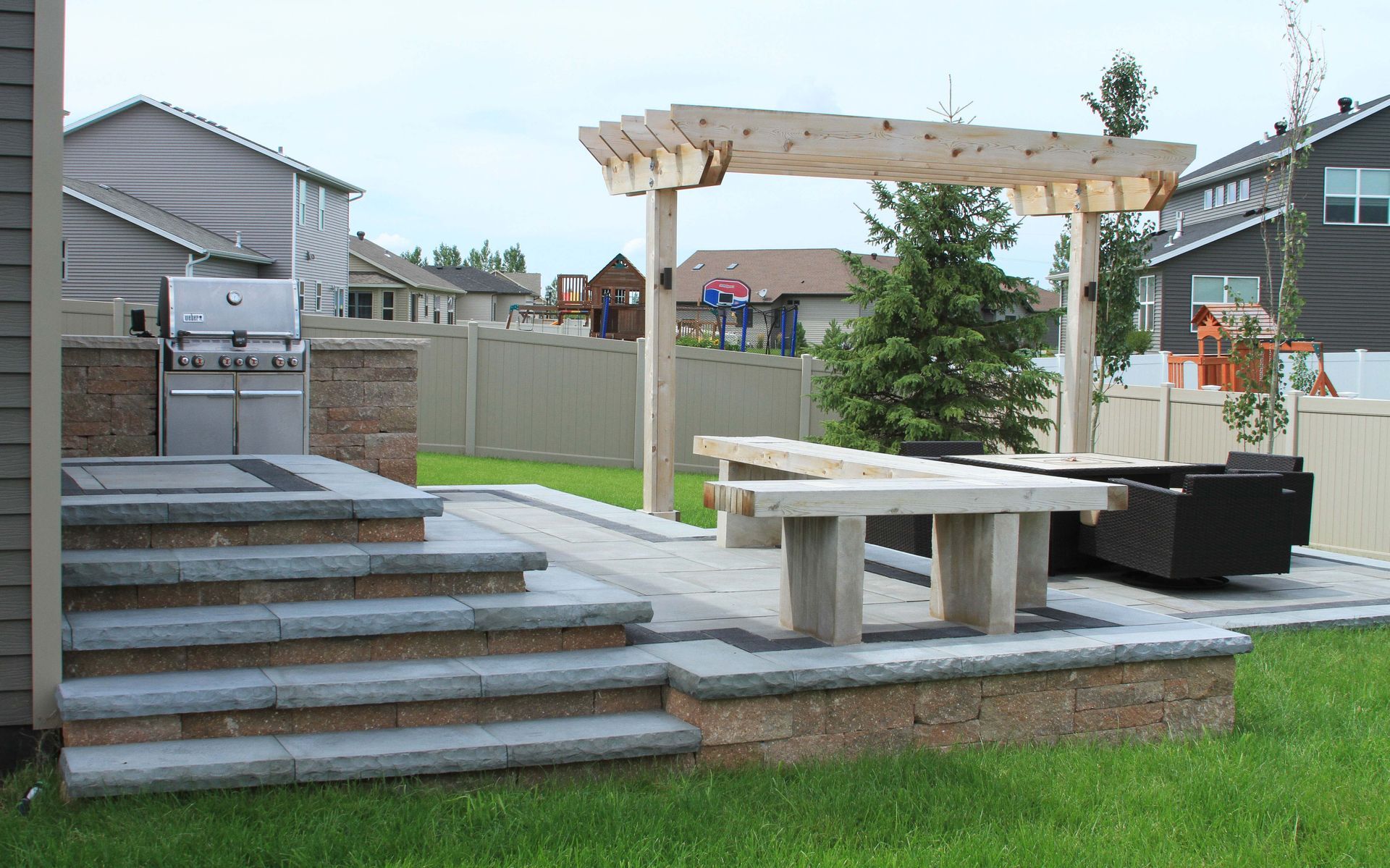 A patio with a grill and a pergola in the backyard