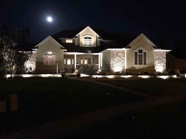 A large house is lit up at night with a full moon in the background