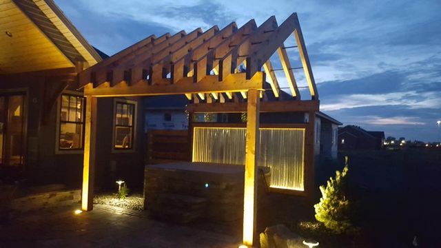 A pergola is lit up at night in front of a house.