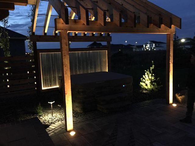 A pergola is lit up at night and has a hot tub underneath it